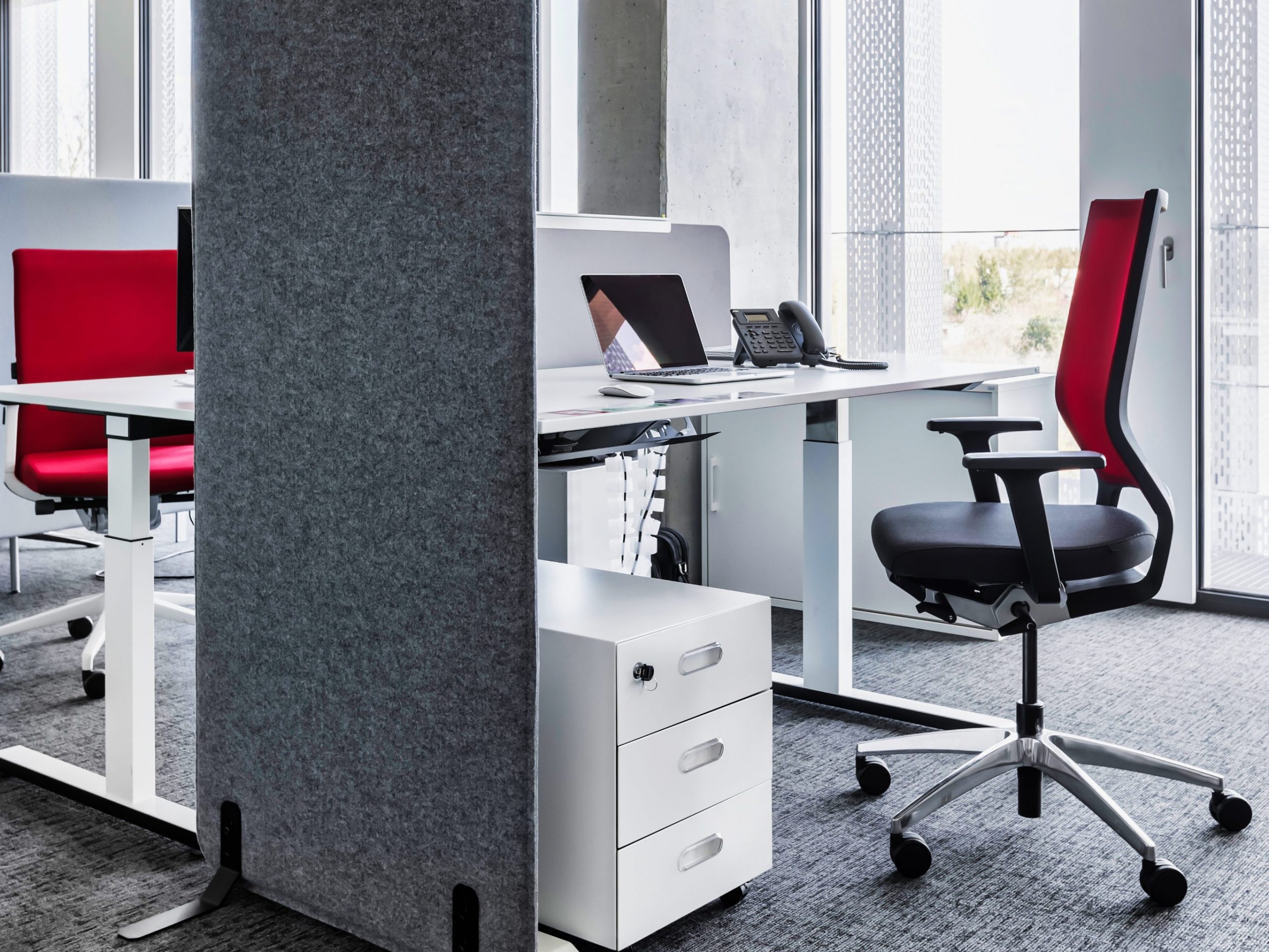 Fokusarbeitsplatz mit elektrisch höhenverstellbaren Tisch in weiß, einer grauen Akustik Standwand und einem Drehstuhl in Schwarz/ Rot 